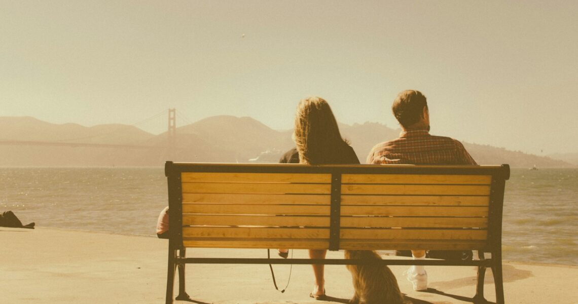man and woman sitting on bench beside body of water